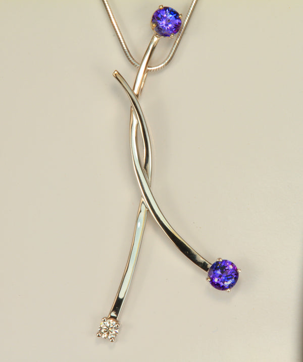 Large uniquely styled pendant with vivid colored tanzanites and ideal cut diamond in 14 kt .white gold